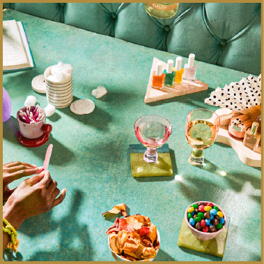 A person is filing their nails at a table filled with nail polish bottles, nail care tools, snacks, and flowers. Description generated by AI