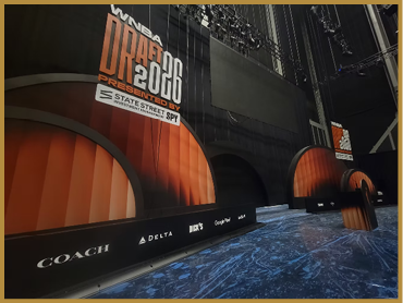 A large indoor stage setup displays signage for the WNBA Draft 2018 presented by State Street SPY with sponsor logos including Coach, Delta, and Dick's. Description generated by AI