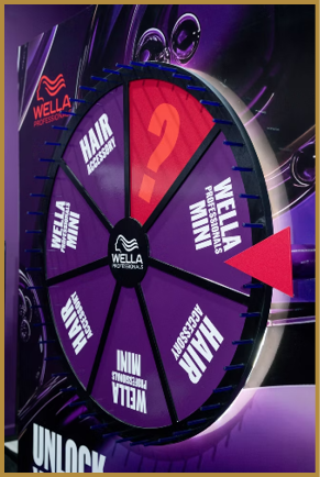 A colorful spinning prize wheel with sections labeled Wella Professionals Mini, Hair Accessory, and a question mark, set against a purple background. Description generated by AI