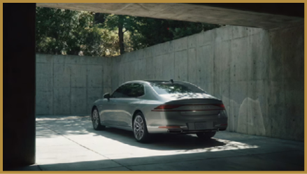 A sleek silver car is parked in a shaded concrete garage with sunlight filtering through the open entrance. Description generated by AI